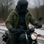 冬の道路で、黒いバイクにまたがったライダーが、軍モノ風のオリーブ色ジャケットと防寒インナーを着込み、黒いジェットヘルメットと手袋でしっかり防寒している様子を写した写真。冷え込む背景の中、冬のバイク装備とレイヤリングの雰囲気が伝わる構図。