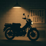 暖色の作業灯に照らされた明るめのガレージで、小型バイクのシルエットが浮かび上がっているオリジナルイラスト。背後には工具が整然と並び、整備スペースの雰囲気がやわらかい光で表現されている。